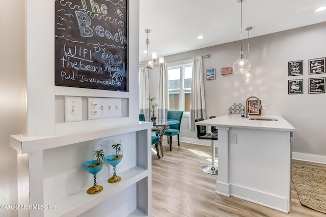 bar featuring pendant lighting, light hardwood / wood-style floors, a chandelier, and sink