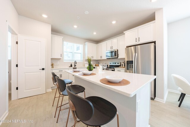 kitchen featuring light hardwood / wood-style flooring, appliances with stainless steel finishes, white cabinets, and a kitchen island with sink