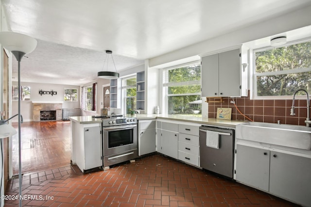 kitchen with appliances with stainless steel finishes, sink, backsplash, kitchen peninsula, and decorative light fixtures