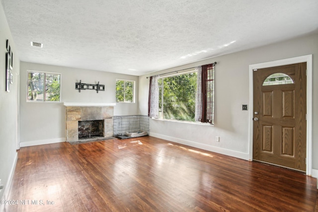 unfurnished living room with a stone fireplace, a textured ceiling, dark wood-type flooring, and a wealth of natural light