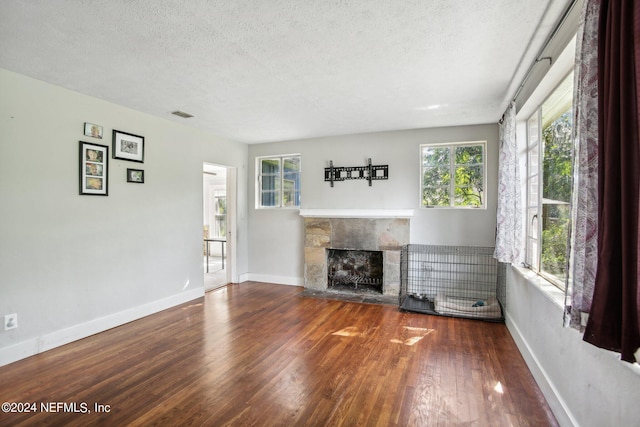 unfurnished living room with a textured ceiling, a stone fireplace, and wood-type flooring