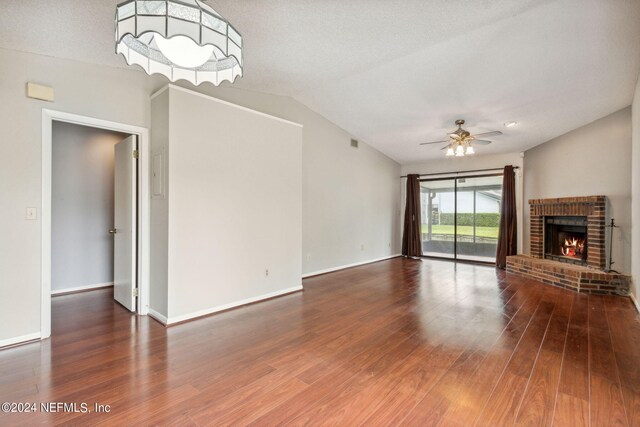 unfurnished living room with a textured ceiling, vaulted ceiling, hardwood / wood-style floors, a brick fireplace, and ceiling fan