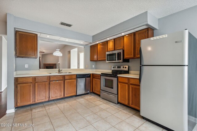 kitchen featuring a textured ceiling, stainless steel appliances, sink, and hanging light fixtures