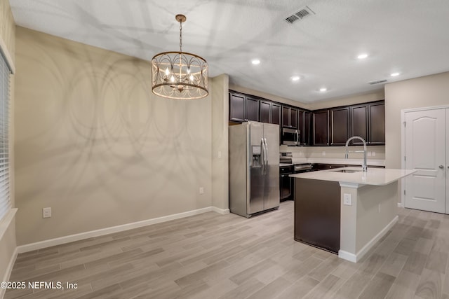 kitchen featuring a kitchen island with sink, appliances with stainless steel finishes, a notable chandelier, sink, and decorative light fixtures