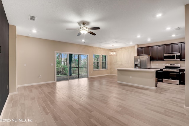 kitchen featuring appliances with stainless steel finishes, light wood-type flooring, a kitchen island with sink, and ceiling fan with notable chandelier