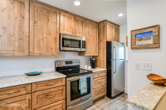 kitchen with a textured ceiling, light stone countertops, appliances with stainless steel finishes, light hardwood / wood-style floors, and decorative backsplash