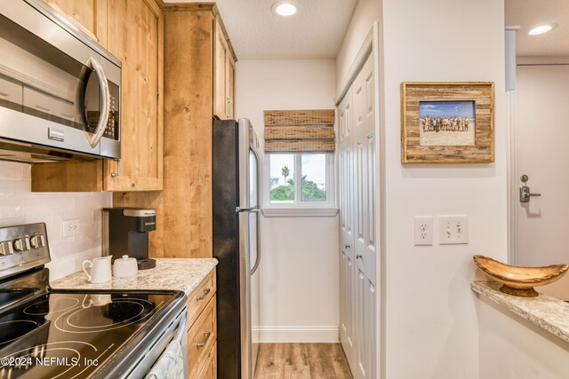 kitchen with a textured ceiling, wood-type flooring, light stone counters, decorative backsplash, and appliances with stainless steel finishes