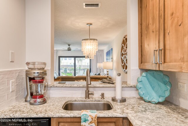 kitchen with a textured ceiling, dishwasher, light stone counters, sink, and hanging light fixtures