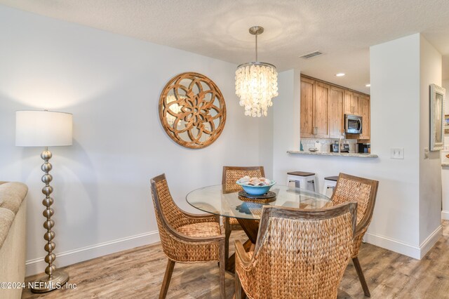 dining area featuring a textured ceiling, light hardwood / wood-style flooring, and an inviting chandelier