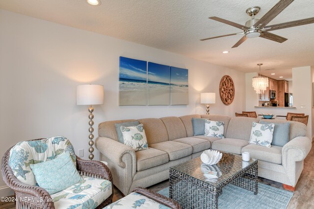 living room with light wood-type flooring, ceiling fan, and a textured ceiling