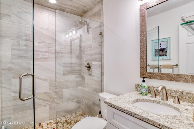 bathroom featuring a shower with shower door, toilet, and vanity