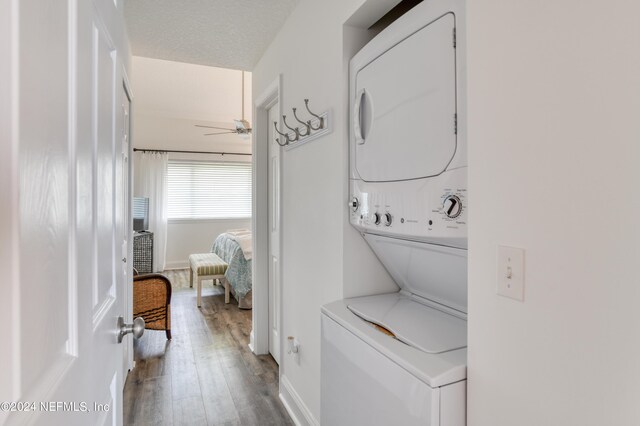 laundry room featuring stacked washer / dryer, a textured ceiling, hardwood / wood-style flooring, and ceiling fan