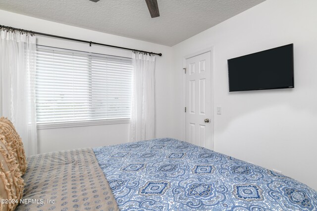 bedroom featuring multiple windows, ceiling fan, and a textured ceiling