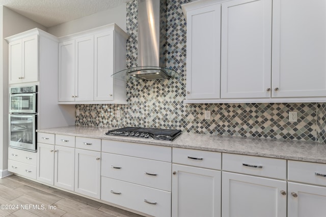 kitchen with wall chimney exhaust hood, appliances with stainless steel finishes, light wood-type flooring, and white cabinetry