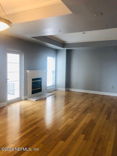 unfurnished living room with a tray ceiling, baseboards, and hardwood / wood-style floors