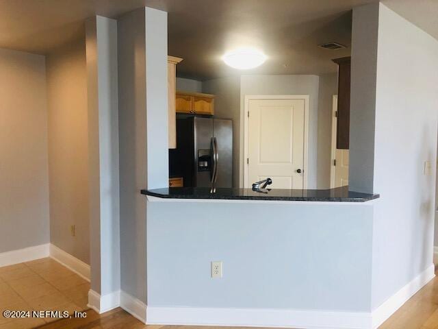 kitchen featuring baseboards, dark countertops, visible vents, a peninsula, and fridge with ice dispenser