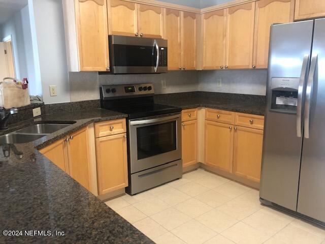 kitchen with dark stone countertops, light brown cabinets, a sink, and stainless steel appliances