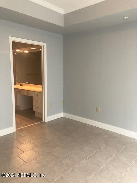 unfurnished bedroom featuring tile patterned floors, ornamental molding, ensuite bath, and baseboards