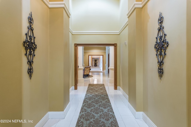 hallway featuring baseboards, a high ceiling, decorative columns, and light tile patterned flooring