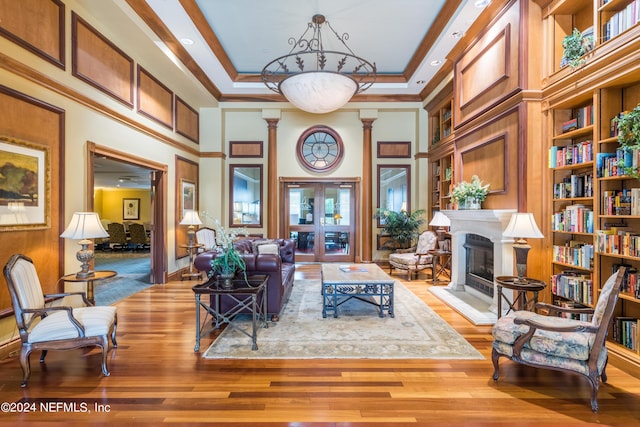 living room with ornamental molding, a fireplace with raised hearth, a raised ceiling, built in features, and wood finished floors