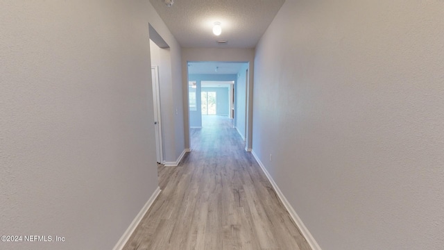 hall with a textured ceiling and light hardwood / wood-style flooring