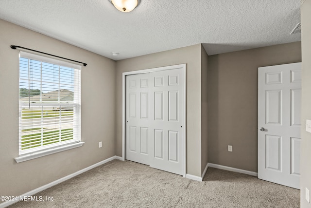 unfurnished bedroom featuring light carpet, a closet, multiple windows, and a textured ceiling