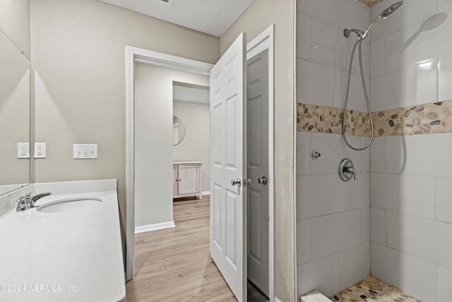 bathroom featuring wood-type flooring, a textured ceiling, vanity, and tiled shower