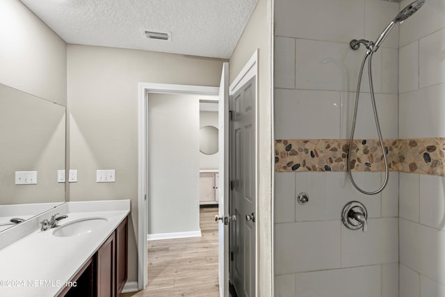 bathroom with wood-type flooring, a textured ceiling, vanity, and tiled shower