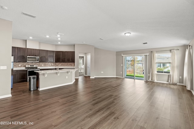 kitchen with a breakfast bar, wood-type flooring, an island with sink, appliances with stainless steel finishes, and dark brown cabinetry