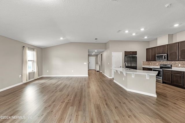 kitchen with a breakfast bar area, stainless steel appliances, lofted ceiling, light hardwood / wood-style flooring, and a kitchen island with sink