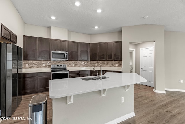 kitchen featuring sink, an island with sink, decorative backsplash, stainless steel appliances, and hardwood / wood-style floors