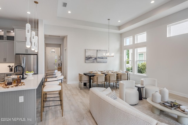 living room featuring sink, light wood-type flooring, a tray ceiling, and a notable chandelier