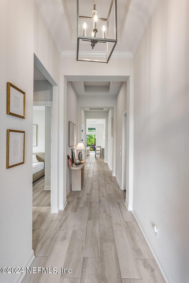 hall with ornamental molding, an inviting chandelier, and light wood-type flooring