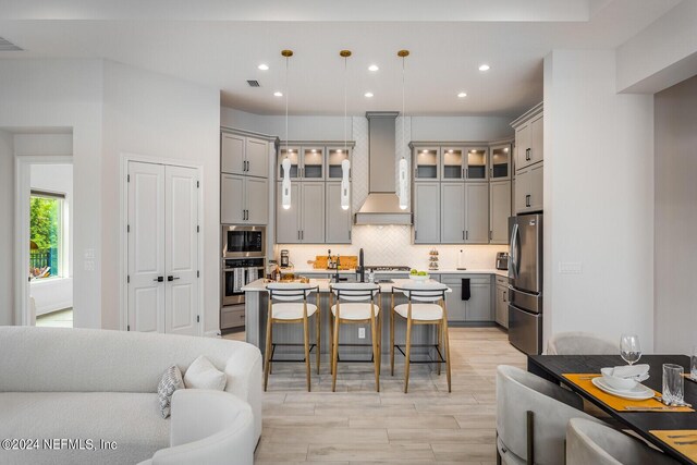 kitchen featuring light hardwood / wood-style flooring, decorative light fixtures, an island with sink, custom range hood, and a breakfast bar area