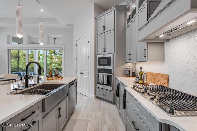 kitchen with decorative light fixtures, stainless steel appliances, sink, custom range hood, and light hardwood / wood-style floors