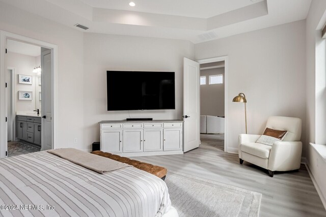 bedroom featuring sink, a tray ceiling, light hardwood / wood-style floors, and ensuite bath