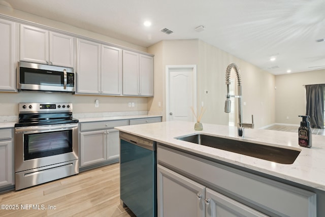 kitchen featuring sink, gray cabinetry, light stone counters, stainless steel appliances, and light wood-type flooring