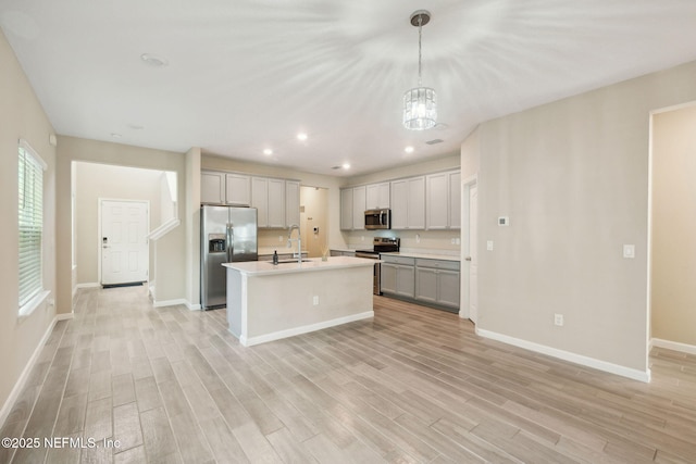 kitchen with pendant lighting, a kitchen island with sink, gray cabinetry, stainless steel appliances, and light hardwood / wood-style floors