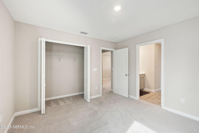 unfurnished bedroom with light colored carpet, a closet, and ensuite bathroom