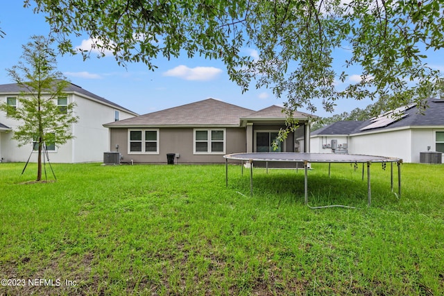 back of property with a trampoline, a lawn, and cooling unit