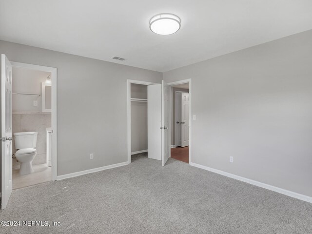 unfurnished bedroom with a closet, carpet, and ensuite bath