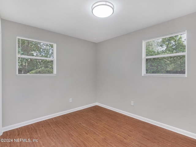 empty room with a wealth of natural light, baseboards, and wood finished floors