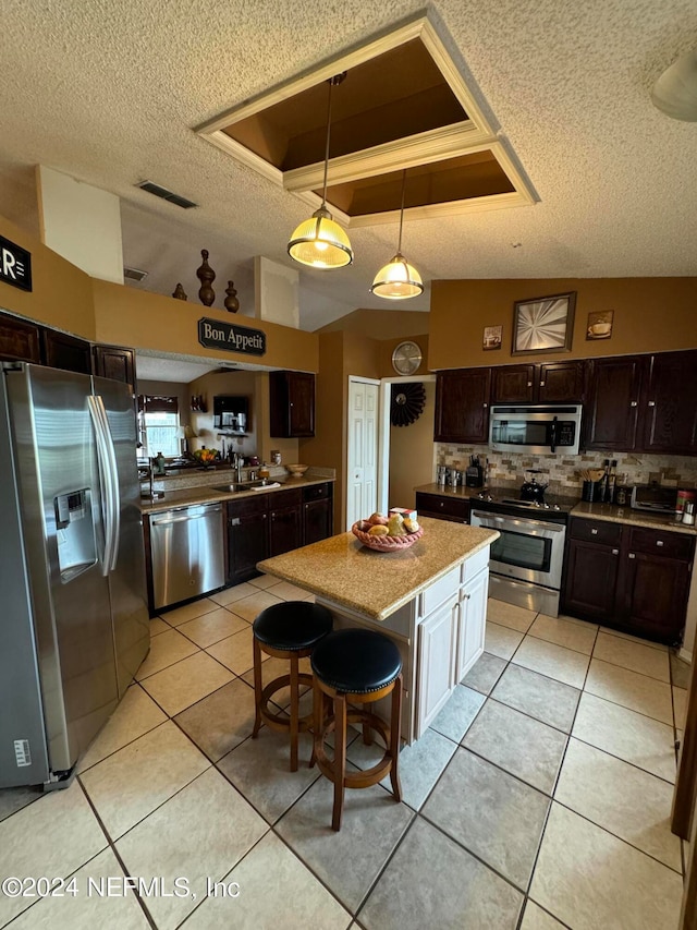 kitchen featuring a textured ceiling, a kitchen island, appliances with stainless steel finishes, a tray ceiling, and dark brown cabinetry