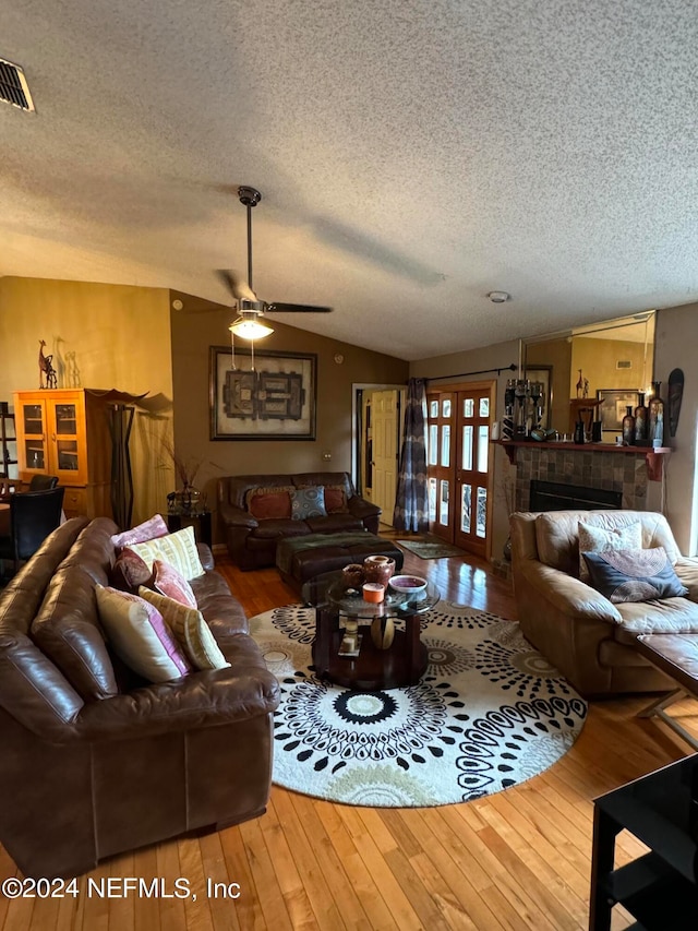 living room with a textured ceiling, a tile fireplace, wood-type flooring, ceiling fan, and lofted ceiling