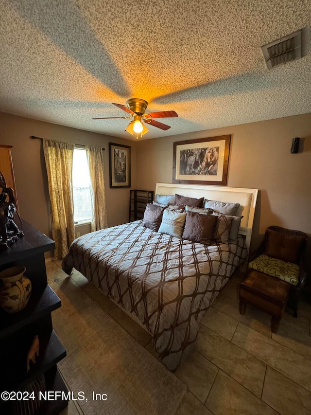 bedroom with tile patterned floors, ceiling fan, and a textured ceiling