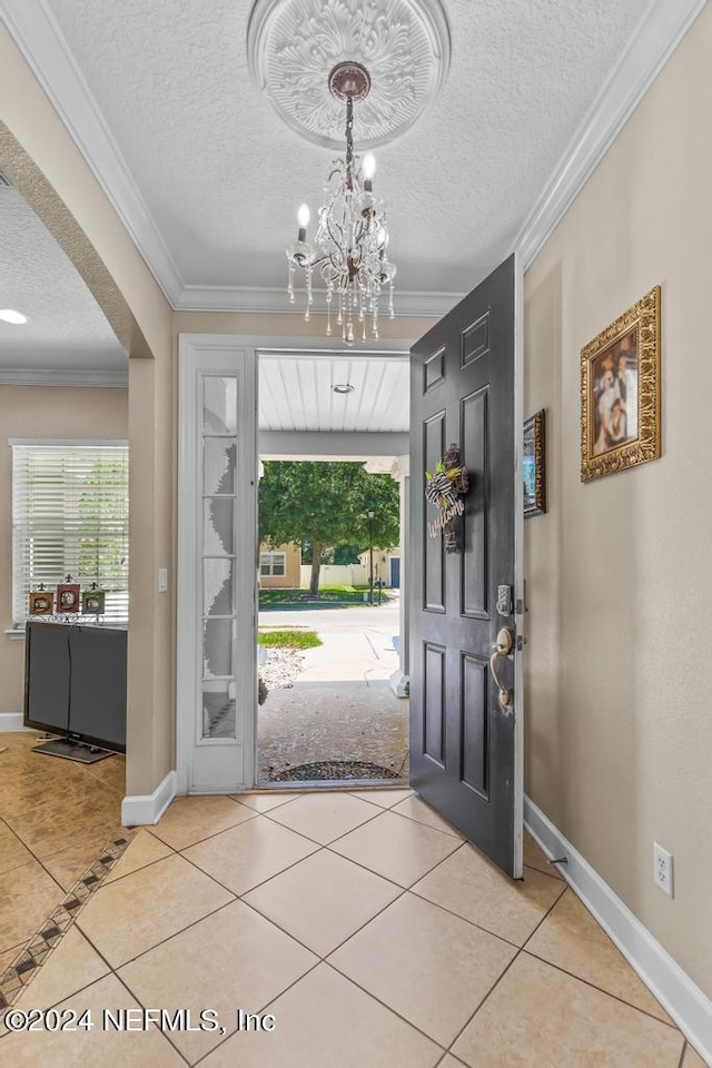 tiled entrance foyer featuring a textured ceiling, crown molding, and a notable chandelier