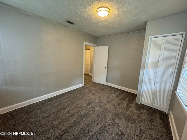 unfurnished bedroom with a textured ceiling, dark carpet, and a closet