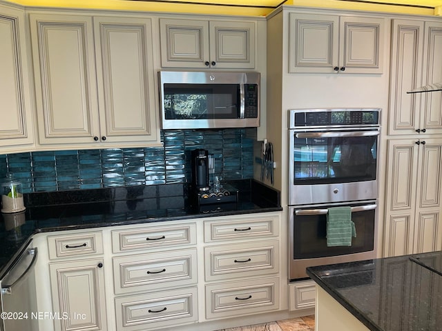 kitchen featuring appliances with stainless steel finishes, decorative backsplash, dark stone countertops, and cream cabinetry