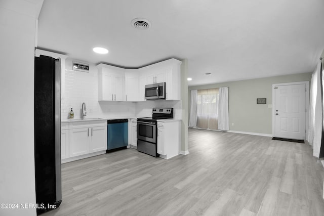 kitchen featuring white cabinets, light wood-type flooring, stainless steel appliances, sink, and decorative backsplash