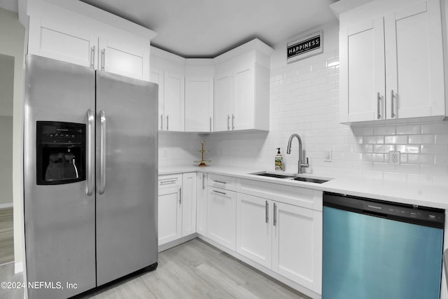 kitchen with appliances with stainless steel finishes, light hardwood / wood-style floors, sink, decorative backsplash, and white cabinets